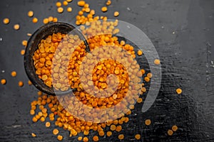 Close up of Raw Masur dal or masoor lentils or pink lentils in a black colored clay bowl on wooden surface.