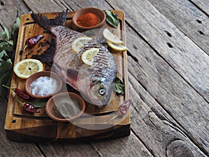 Close-up. Raw river fish of bream cooked for baking in the oven with slices of lemon and seasoning on a wooden board.Front view