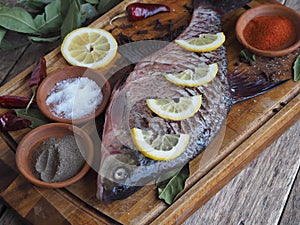 Close-up. Raw river fish of bream cooked for baking in the oven with slices of lemon and seasoning on a wooden board.Front view