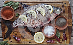 Close-up. Raw river fish of bream cooked for baking in the oven with slices of lemon and seasoning on a wooden board.Side view