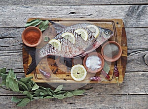 Close-up. Raw river fish of bream cooked for baking in the oven with slices of lemon and seasoning on a wooden board. Side view.