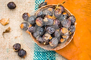 Close up of raw soap nuts in a clay bowl on brown colored surface.