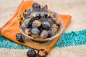 Close up of raw soap nuts in a clay bowl on brown colored surface.