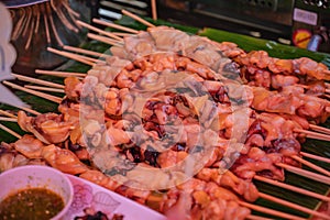 Close up raw squid meat skewer on banana leaf in the fresh market of thailand with spicy seafood sauce.