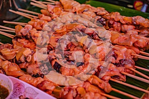 Close up raw squid meat skewer on banana leaf in the fresh market of thailand with spicy seafood sauce.