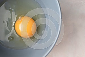 Close-up raw uncooked egg in gray bowl with copy space, top view. Yellow egg yolk and liquid egg whites. Ingredient for baking