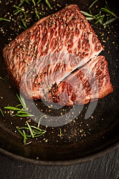 Close up raw wagyu beef striploin steak with pepper on dark pan. Restaurant