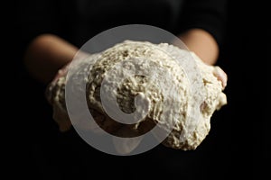 Close-up, raw yeast dough in hands on a black background