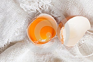 Close up of raw yolk in eggshell on white linen background