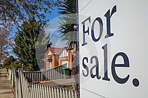 Close up of a real estate sign board with text  `for sale` , some suburban houses/Australian homes and pedestrian walkway as