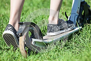 Close-up rear view of child riding kick scooter, green grass on summer meadow