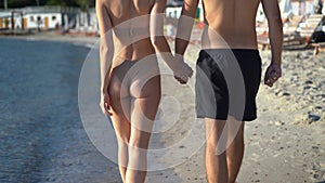 close-up rear view of couple walking on the beach. Young happy couple walking on the beach smiling holding each other