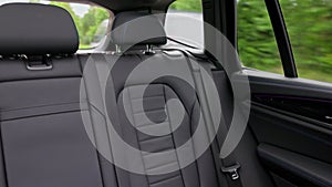 Close-up of rear view interior with leather seats of new black electric car driving on highway.