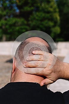 Close-up rear view of a male head with thinning hair or alopecia with one hand on the nape of his neck