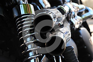 Close up rear view of a powerful classic black vintage motorcycle showing suspension and shiny chrome exhaust pipes