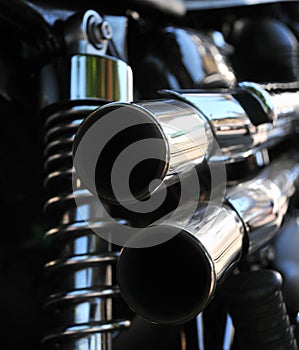 Close up rear view of a powerful classic black vintage motorcycle showing suspension and shiny chrome exhaust pipes