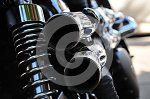 Close up rear view of a powerful classic black vintage motorcycle showing suspension and shiny chrome exhaust pipes