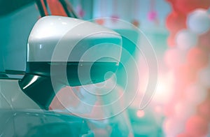 Close-up rear view wing mirror of luxury car on blurred background of modern showroom decor with red and white balloons. Auto