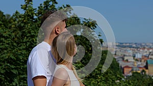 Close up. Rear of young Caucasian happy couple man and woman hugging and looking away at city landscape background while