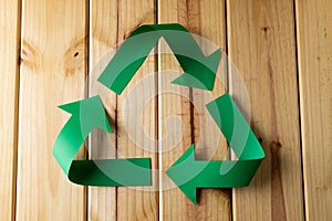 Close up of recycling symbol of paper green arrows on wooden background with copy space