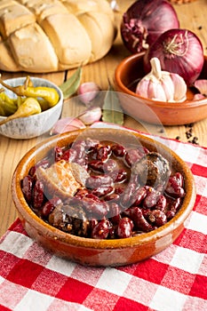 Close-up of red bean stew on red kitchen cloth, rustic wooden table with green chillies, garlic, onions,