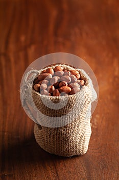 Close-up of red-brown peanuts Arachis hypogaea in a standing jute bag over wooden brown background