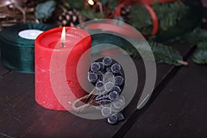 Close-up of a red burning candle and artificial black berries for a Christmas wreath, festive decor, selective focus