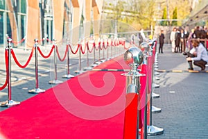 Close up red carpet ceremony with selective focus on the stanchions and the ropes with blurred guests and photographer background.