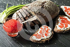 Close-up red caviar in bowl and Sandwiches on wooden cutting board on black background.