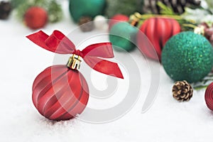 Close up red christmas ball, bauble with ribbon and green fir branches, pine cones, on white snow background. Winter holidays.