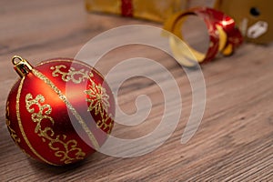 Close-up of a red christmas bulb with a gift box and wrapping tape in background on a wooden table