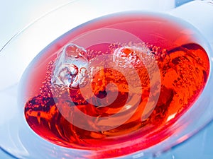 Close-up of red cocktail drink with ice cubes on blue light tint background, fun and dance disco