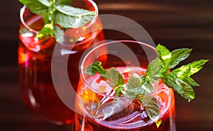 Close up of red cocktail with ice cubes green mint leaves in wine glass