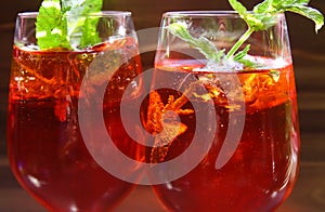 Close up of red cocktail with ice cubes green mint leaves in wine glass