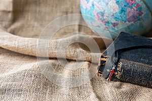 Close up of the red cross on the old holy bible and world globe on vintage linen sack cloth background