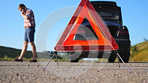 Close up of red emergency stop sign standing on road. Worried and angry driver walking near his broken car talking on