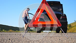 Close up of red emergency stop sign standing on road. Worried and angry driver walking near his broken car talking on