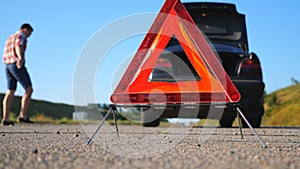 Close up of red emergency stop sign standing on road. Worried and angry driver walking near his broken car talking on