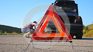 Close up of red emergency stop sign standing on road. Worried and angry driver walking near his broken car talking on