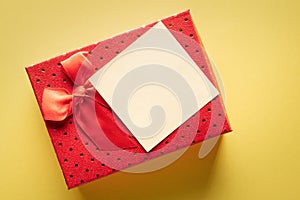 Close up of a red gift box with a blank note on a yellow background: concept of giving or reminder