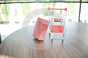 Close up red gift box and shopping cart on table for shopping and e-commerce concept