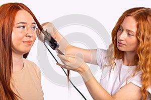 Close-up of red-haired caucasian girls. Hairdressing, high temperature hair straightening. White background.