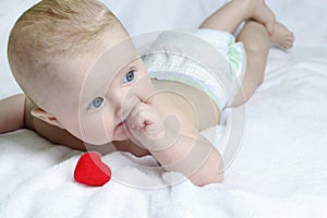 Close-up of a red heart and a cute baby lying on a white towel. Chew and suck on your fingers. Copy space - toothache concept,