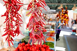 Close up of red hot chili pepper hangin at organic farmers market stalls with people in background during sunny summer day photo