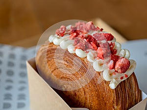 Close-up red iced strawberries and soft cream on brown cake or croissant bread.