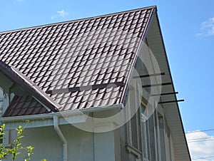 Close up on red metal roof with white, plastic rain gutter system. Roofing Construction.