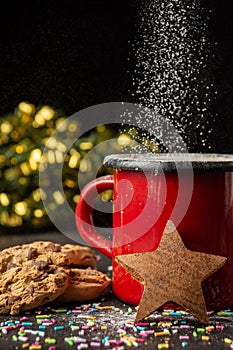 Close-up of red mug with chocolate and star with falling sugar, on table with cookies and Christmas decoration, selective focus