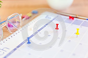 Close-up red pin on blank desk calendar with office equipment concept of event planner or personal organization for