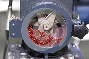 Close up red plastic granules in crusher machine with blade of cutting prepare material for injection process