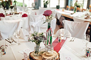 Close up of red rose flower in decorated high glass vase and arrangement of glassware. Festive table decoration